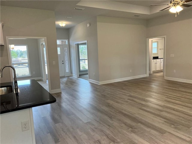 unfurnished living room with visible vents, a ceiling fan, a sink, wood finished floors, and baseboards