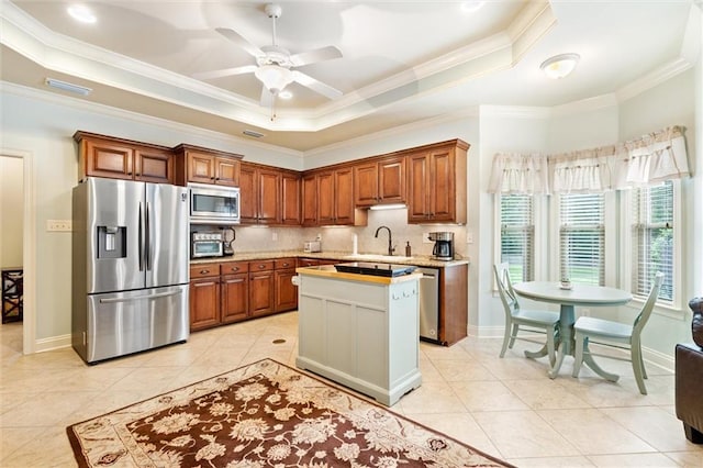 kitchen featuring a sink, ceiling fan, light countertops, stainless steel appliances, and a raised ceiling