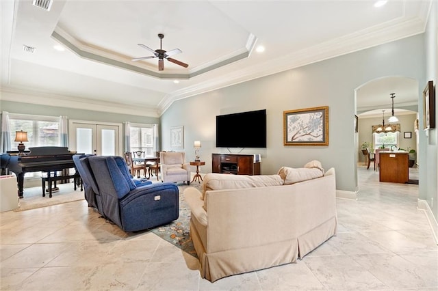 living area with a tray ceiling, visible vents, crown molding, and ceiling fan with notable chandelier