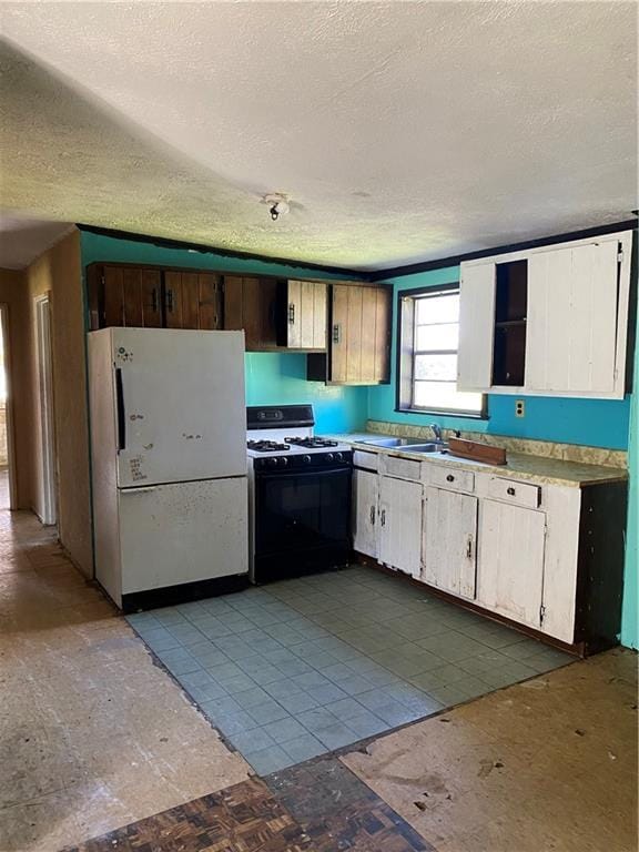 kitchen featuring light countertops, a textured ceiling, range with gas stovetop, a sink, and freestanding refrigerator