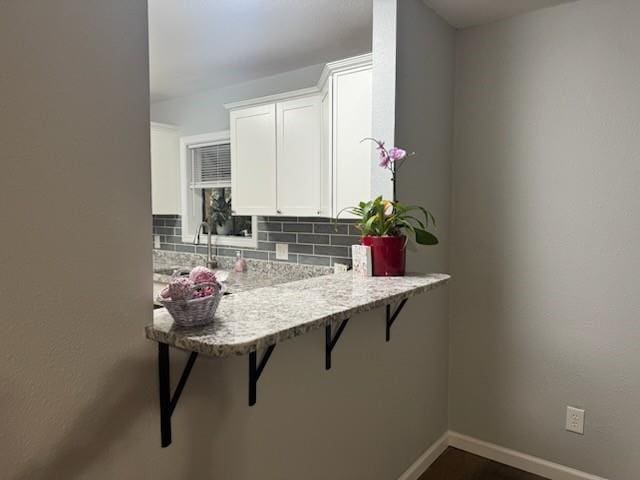 kitchen featuring backsplash, light stone countertops, a breakfast bar, and white cabinets