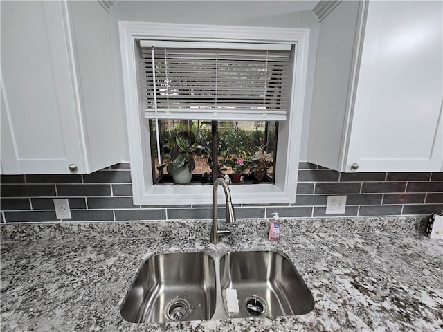 room details with tasteful backsplash, light stone countertops, sink, and white cabinets