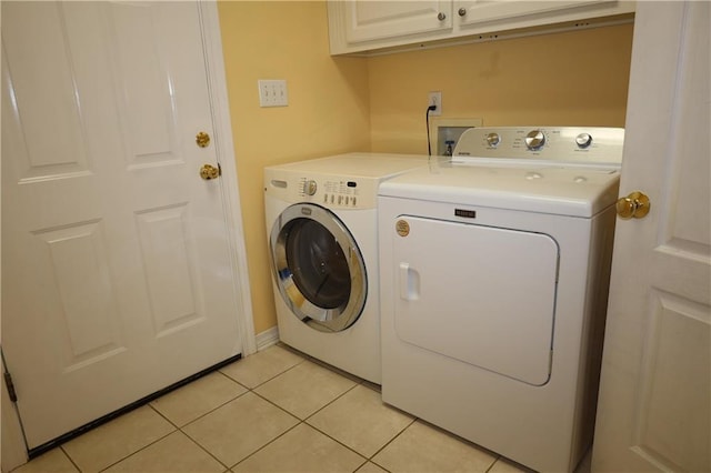 washroom with light tile patterned floors, washing machine and dryer, and cabinet space