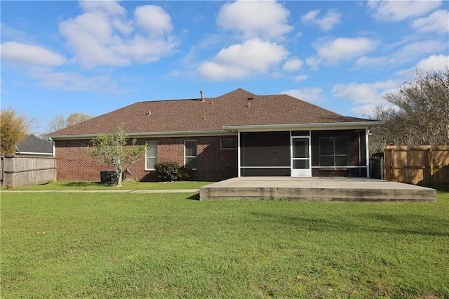 rear view of house featuring brick siding, a shingled roof, fence, a yard, and a sunroom