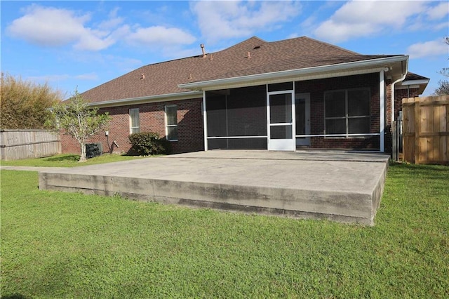 rear view of house with a lawn, a sunroom, fence, a shingled roof, and brick siding