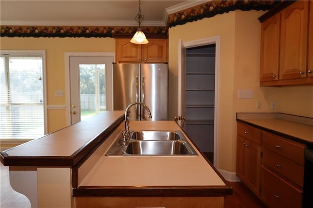 kitchen with decorative light fixtures, a center island with sink, ornamental molding, freestanding refrigerator, and a sink