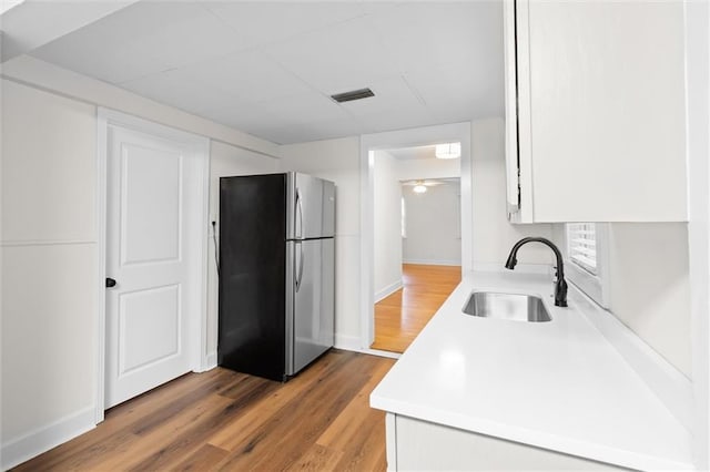 kitchen featuring wood-type flooring, white cabinetry, stainless steel refrigerator, and sink