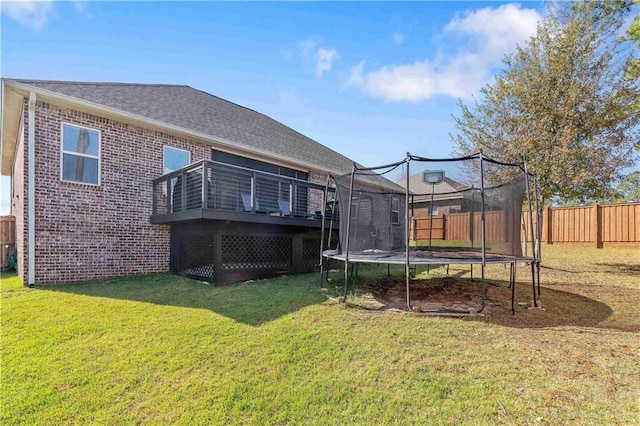 back of house featuring a yard, a deck, and a trampoline