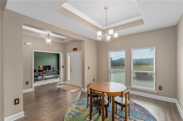 dining space with an inviting chandelier, ornamental molding, dark wood-type flooring, and a tray ceiling