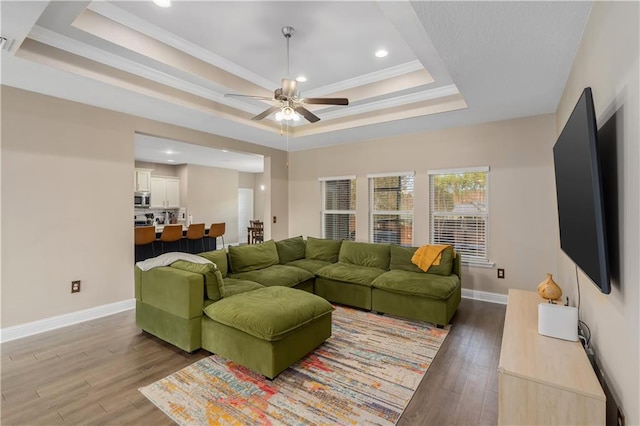 living room featuring hardwood / wood-style flooring, a raised ceiling, ceiling fan, and ornamental molding