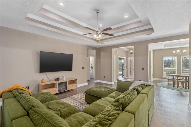 living room featuring hardwood / wood-style flooring, ceiling fan with notable chandelier, a raised ceiling, and ornamental molding