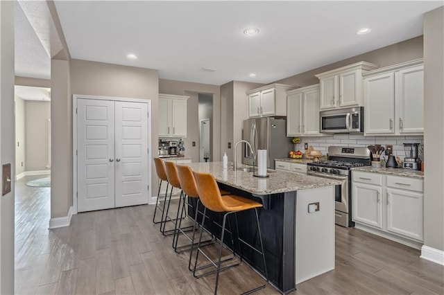 kitchen featuring light stone countertops, a kitchen breakfast bar, stainless steel appliances, a kitchen island with sink, and white cabinets