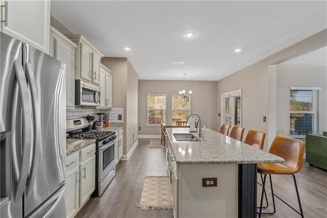 kitchen featuring appliances with stainless steel finishes, a kitchen island with sink, sink, pendant lighting, and a breakfast bar area