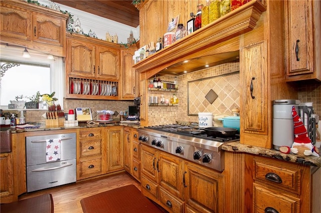 kitchen featuring decorative backsplash, dark stone countertops, light wood-type flooring, and stainless steel gas stovetop