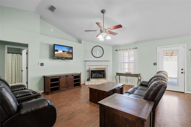 living room featuring a tile fireplace, ceiling fan, dark hardwood / wood-style flooring, and vaulted ceiling