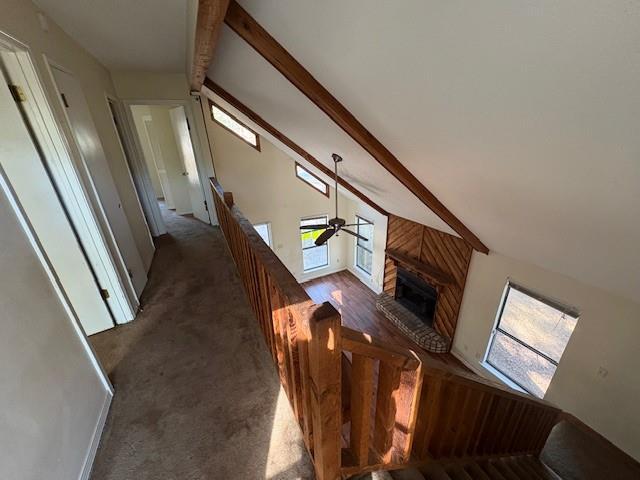 unfurnished living room featuring ceiling fan, dark carpet, a brick fireplace, and vaulted ceiling with beams