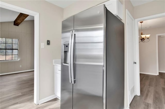 kitchen with stainless steel fridge, an inviting chandelier, light wood-type flooring, beam ceiling, and white cabinetry