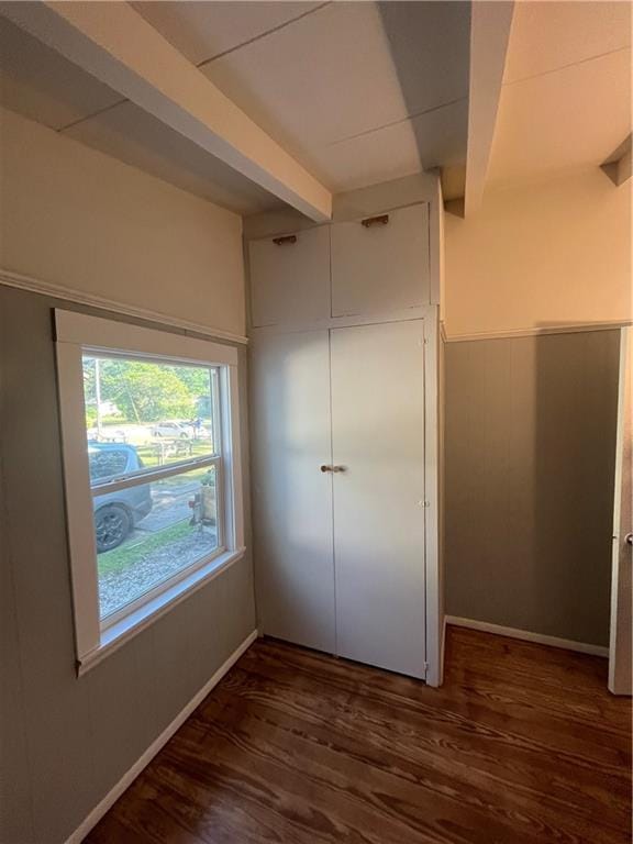 unfurnished bedroom featuring baseboards, beam ceiling, and wood finished floors