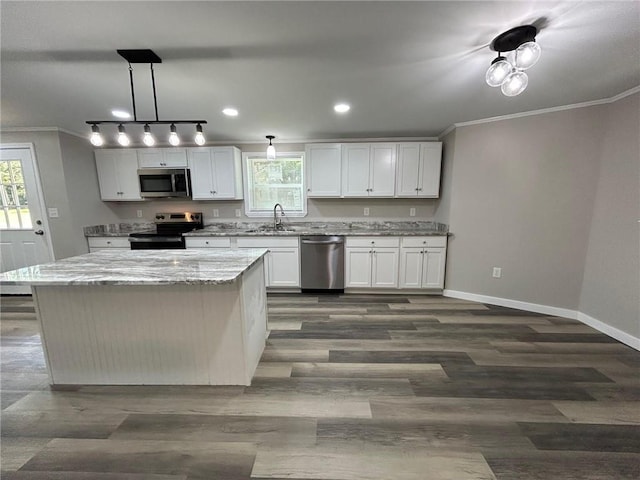 kitchen with a kitchen island, appliances with stainless steel finishes, a sink, baseboards, and ornamental molding