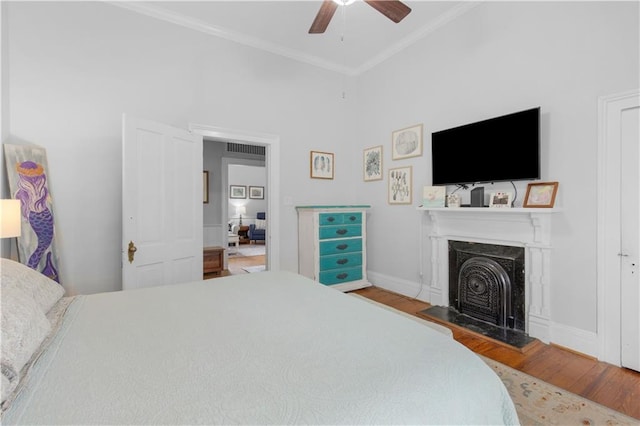 bedroom featuring ceiling fan, wood finished floors, a high end fireplace, baseboards, and ornamental molding