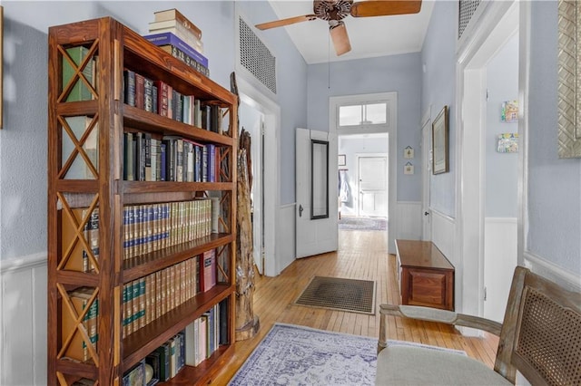 hall with light wood finished floors, visible vents, and wainscoting