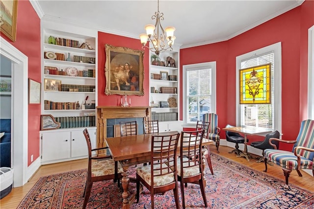 dining area with light wood-style floors, a notable chandelier, crown molding, and built in shelves