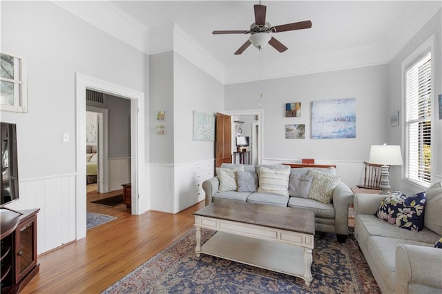 living area with visible vents, a wainscoted wall, ceiling fan, wood finished floors, and crown molding