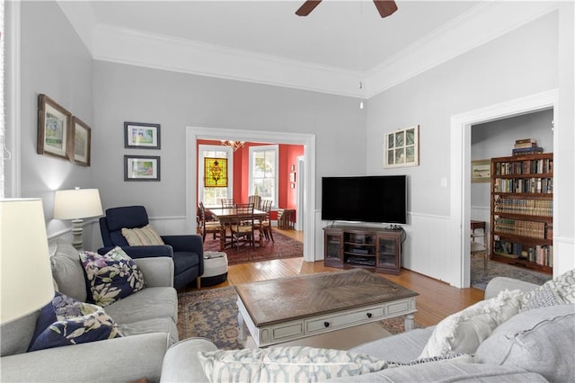 living area with crown molding, ceiling fan, wood finished floors, and wainscoting