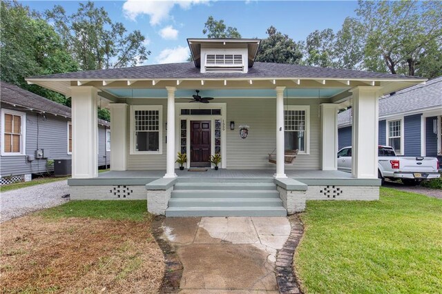 bungalow-style home with ceiling fan, cooling unit, covered porch, and a front lawn