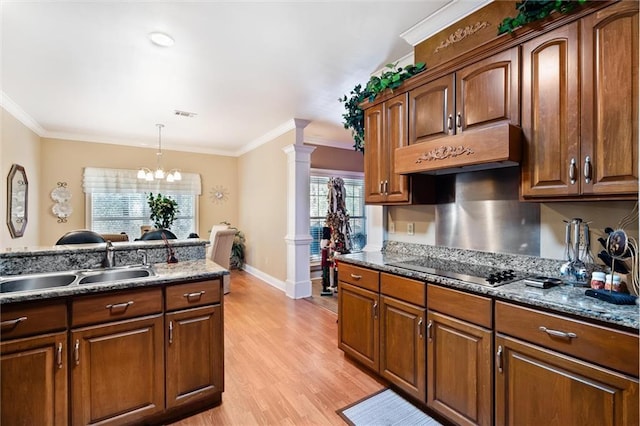 kitchen featuring ornate columns, dark stone counters, sink, an inviting chandelier, and hanging light fixtures