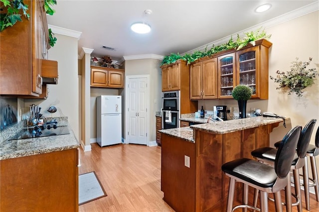 kitchen featuring black electric stovetop, light hardwood / wood-style flooring, ornamental molding, double oven, and white fridge