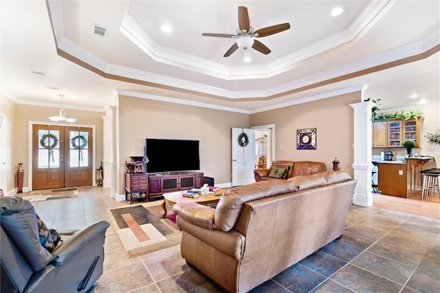 living room with french doors, decorative columns, ceiling fan with notable chandelier, a raised ceiling, and crown molding