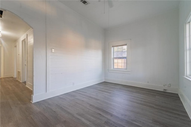 unfurnished room with dark wood-style floors, visible vents, arched walkways, and baseboards