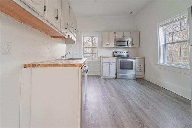 kitchen featuring light wood finished floors, wood counters, baseboards, and stainless steel appliances