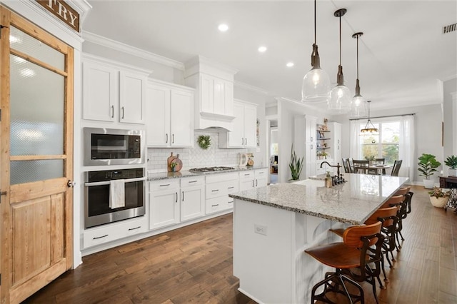 kitchen with white cabinetry, hanging light fixtures, a kitchen island with sink, and appliances with stainless steel finishes