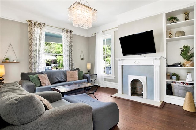 living room with a healthy amount of sunlight, a fireplace with raised hearth, an inviting chandelier, and wood finished floors