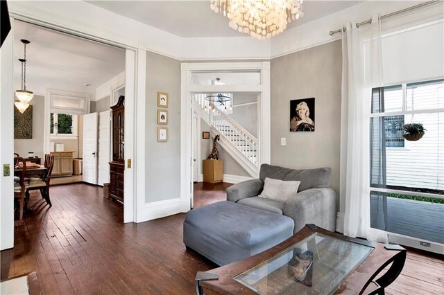 living area with a chandelier, stairs, dark wood-style flooring, and baseboards
