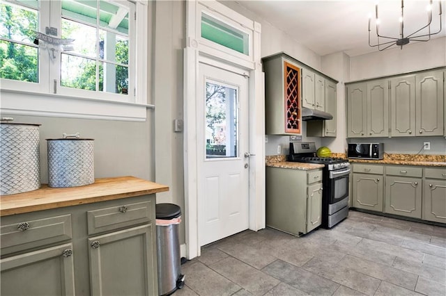 kitchen with stainless steel range with gas stovetop, plenty of natural light, an inviting chandelier, under cabinet range hood, and gray cabinets