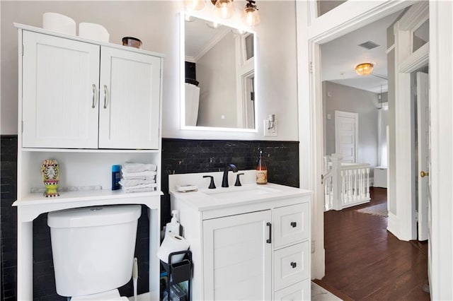 bathroom featuring visible vents, toilet, vanity, wood finished floors, and backsplash