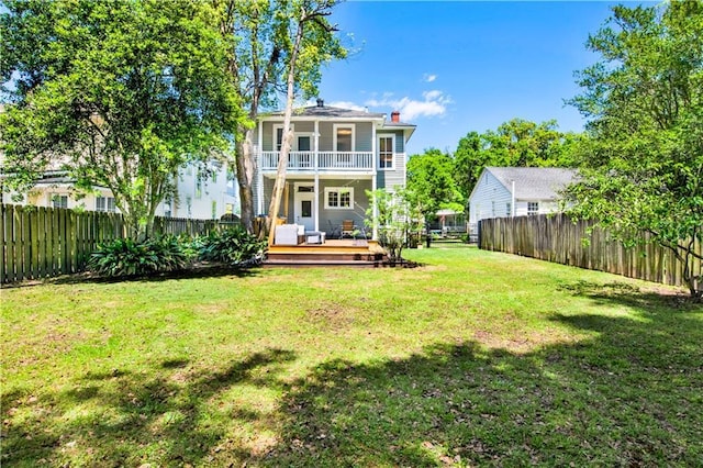rear view of property featuring a balcony, a chimney, a fenced backyard, a yard, and a deck