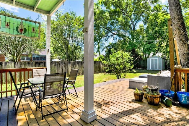 wooden deck featuring outdoor dining space, a shed, a fenced backyard, an outbuilding, and a yard