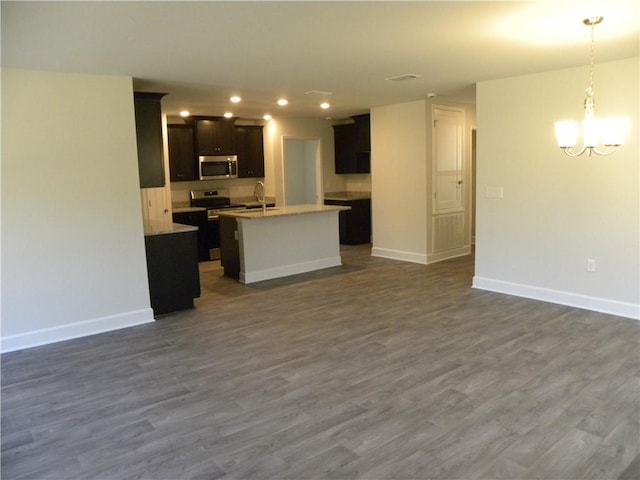 kitchen with sink, dark wood-type flooring, stainless steel appliances, decorative light fixtures, and a center island with sink