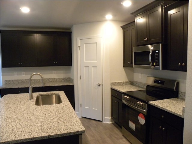 kitchen featuring a kitchen island with sink, sink, appliances with stainless steel finishes, light hardwood / wood-style floors, and light stone counters