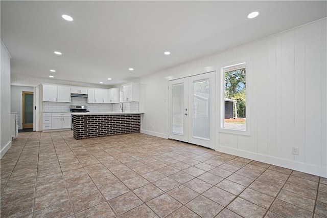 kitchen featuring white cabinetry, sink, stainless steel range oven, backsplash, and light tile patterned floors