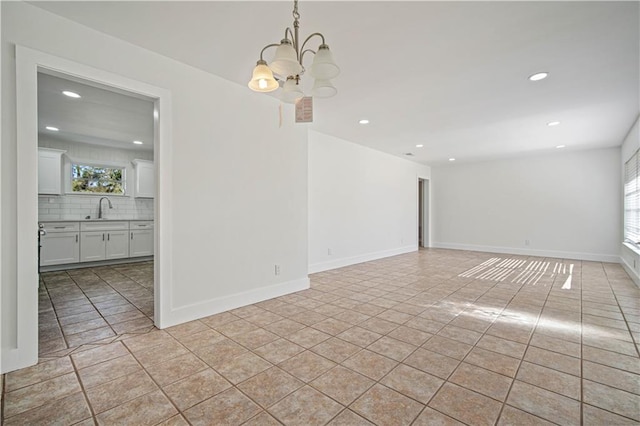 tiled empty room featuring a healthy amount of sunlight, sink, and a chandelier