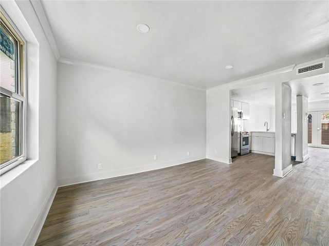 unfurnished living room with sink, ornamental molding, and light hardwood / wood-style floors