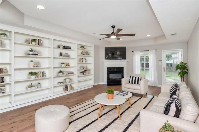 unfurnished living room featuring ceiling fan, wood-type flooring, a premium fireplace, and a tray ceiling