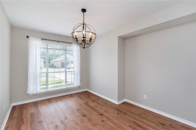 spare room featuring wood-type flooring, a wealth of natural light, and an inviting chandelier