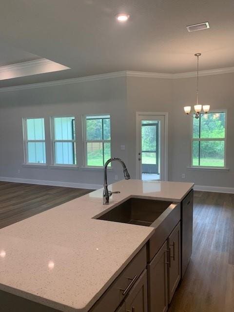 kitchen with a kitchen island with sink, light stone counters, decorative light fixtures, and sink