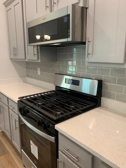 kitchen featuring appliances with stainless steel finishes, gray cabinetry, backsplash, light stone countertops, and light wood-type flooring